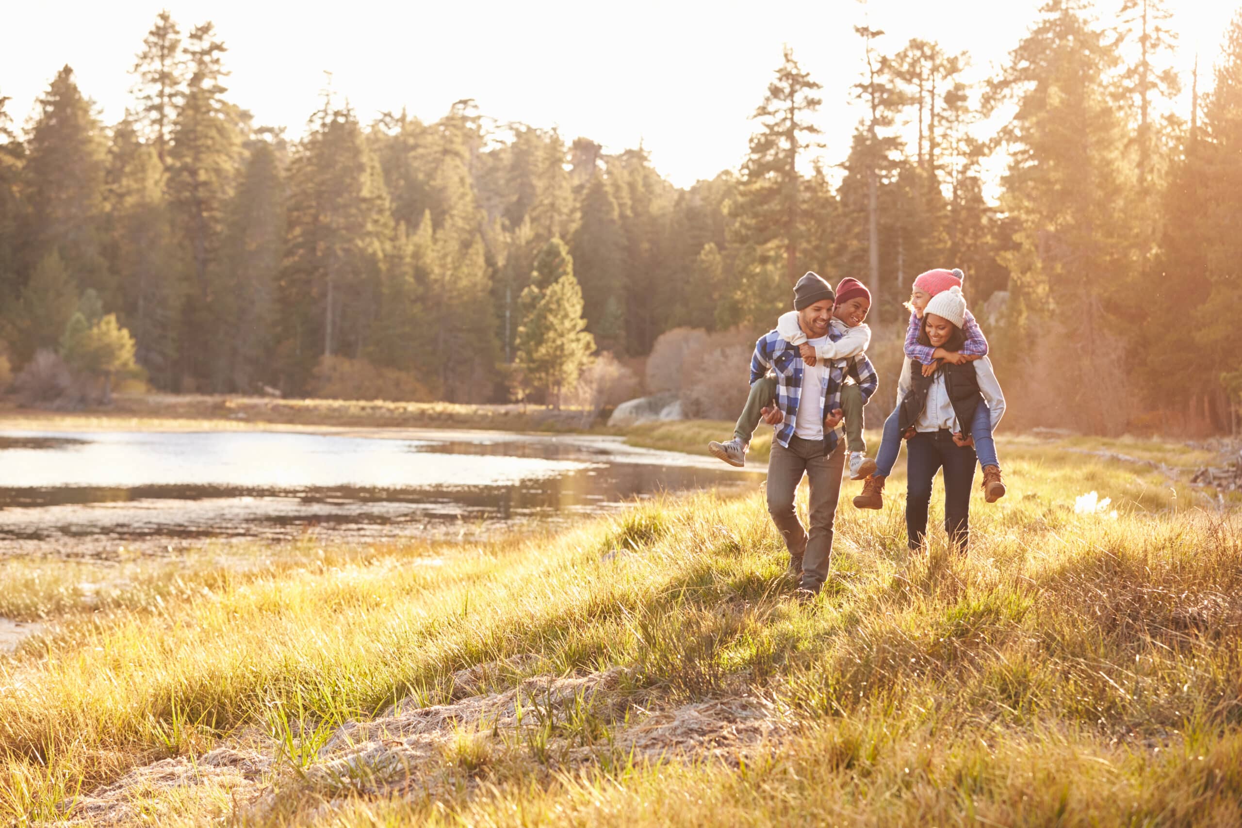 Parents Giving Children Piggyback Ride On Walk By Lake